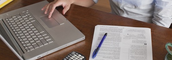 Woman Working on Laptop Computer, Calculator at Dining Room Table