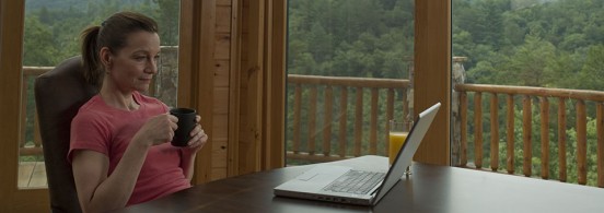 Woman sitting at desk, holding mug, reading from laptop